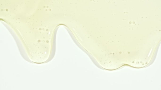 黄色透明化妆品凝胶流体与分子气泡流动在普通白色表面。微距镜头