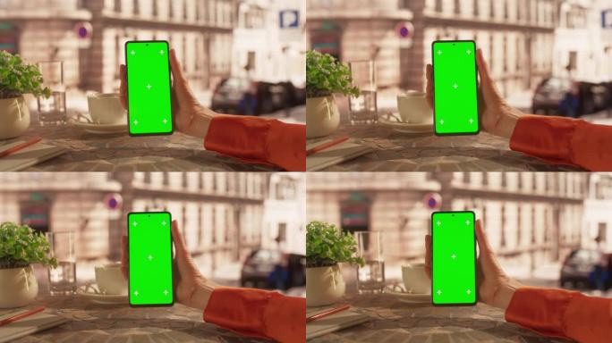 一位匿名女商人手持绿屏模拟显示屏的智能手机，在户外咖啡馆观看视频。虚拟会议，视频通话，电影流概念