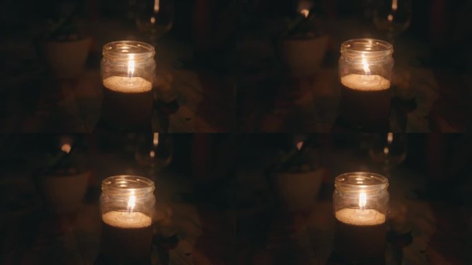 黑暗中木桌上的玻璃罐里燃着蜡烛。舒缓舒适的视频蜡烛火焰冥想。黑暗中闪烁着温暖的火焰