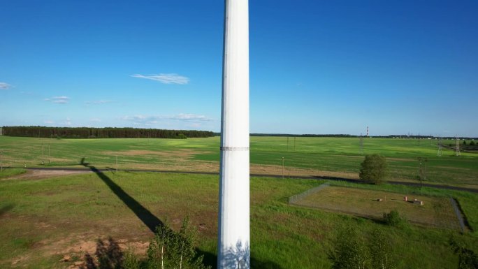 航拍画面显示，在郁郁葱葱的绿色田野中，风力涡轮机的叶片在风中优雅地转动，在阳光下投下清晰的阴影