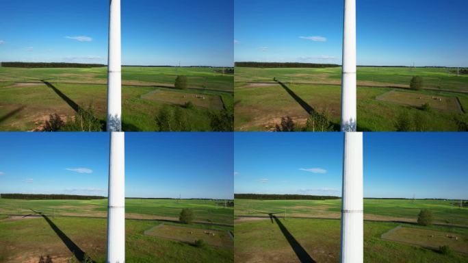 航拍画面显示，在郁郁葱葱的绿色田野中，风力涡轮机的叶片在风中优雅地转动，在阳光下投下清晰的阴影
