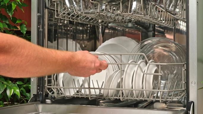 男人拿出洗碗机的篮子，卸下干净的盘子。洗涤循环后，洗碗机释放。