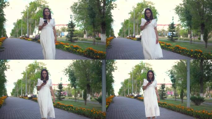 一位年轻女子手里拿着电话走在花巷里。一个穿白裙子的女孩看着她的手机，走在花丛中。4 k