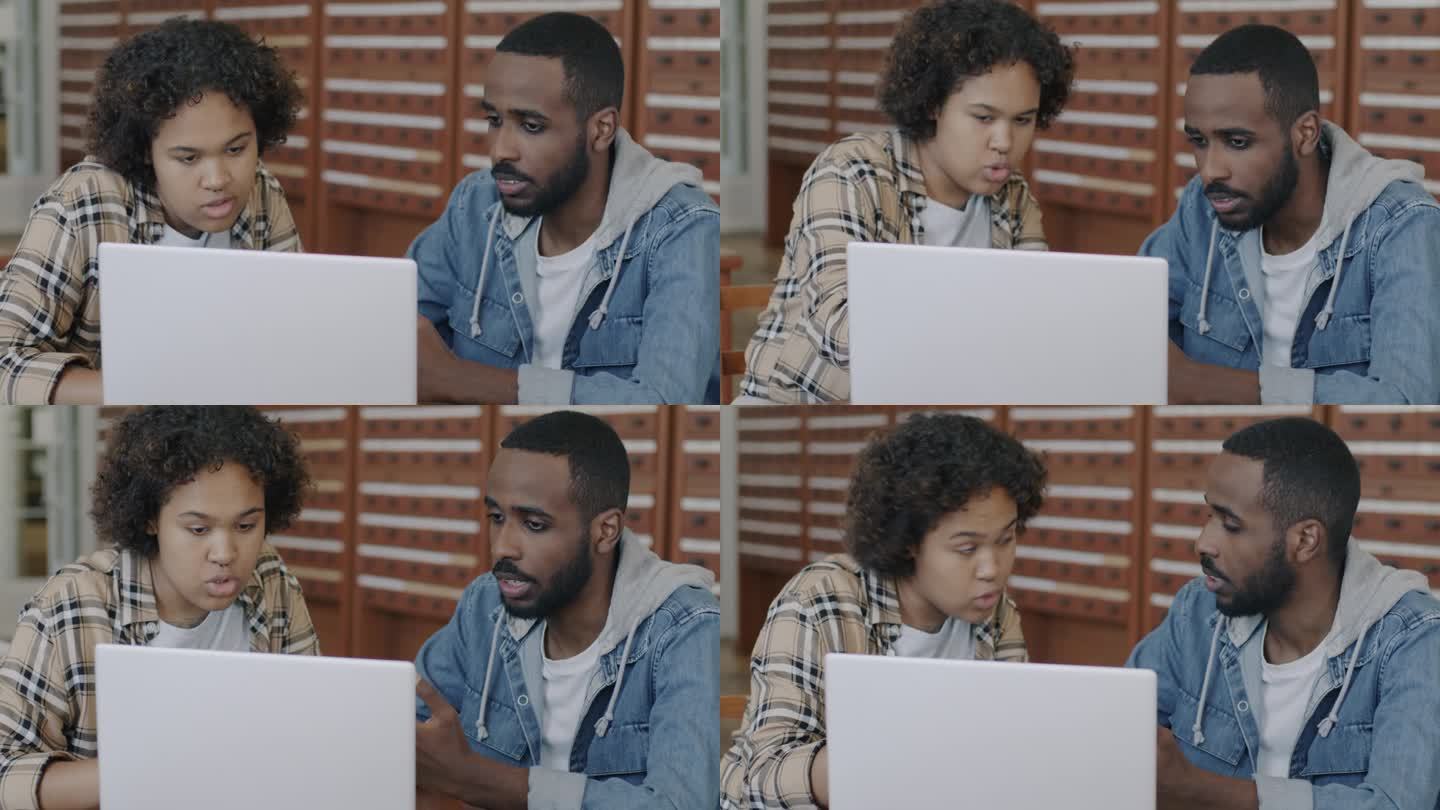 两名非裔美国学生，一男一女，在图书馆大厅用笔记本电脑工作，边说边看屏幕