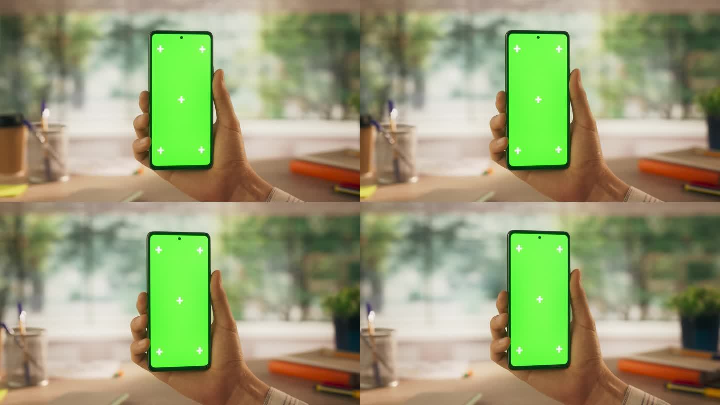 匿名商人拿着绿屏模拟显示屏的智能手机，在创意办公环境中进行视频通话。虚拟会议、现代技术与远程工作概念