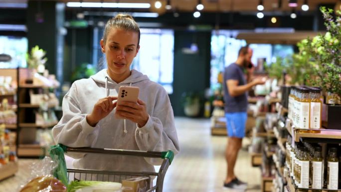 美丽的女运动员在超市用智能手机查看购物清单