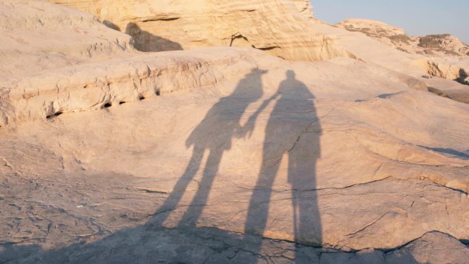在金色的夕阳下，一对情侣手拉手在白色的岩石上跳舞。一男一女在日落时分享受户外度假的休闲时光。