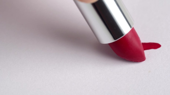 一个女人的手用红色的口红在白色的背景上做了一个记号。化妆品唇彩，唇膏涂抹，涂抹，描边。在白色背景上涂