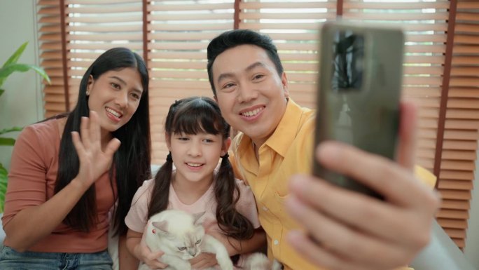 与亚洲中年父亲的全家福，他正微笑着自拍。6岁的亚洲女孩抱着一只白色的小猫，和爸爸妈妈一起拍全家福。