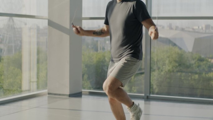 倾斜的肖像肌肉发达的年轻人训练跳绳在美丽的阳光健身房