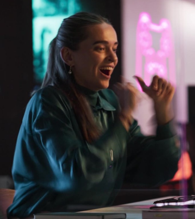 垂直屏幕:晚上在游戏开发公司坐在电脑前的富有表现力的女性。兴奋的制作人很高兴并庆祝她的电子游戏获得好