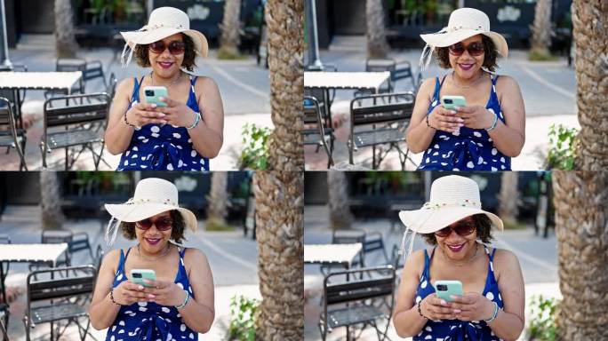 年轻美丽的拉丁女子游客戴着夏天的帽子和太阳镜在咖啡厅露台上使用智能手机