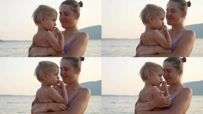 夕阳下的沙滩上，穿着比基尼的微笑女子抱着她的儿子。假期、暑假、旅游。