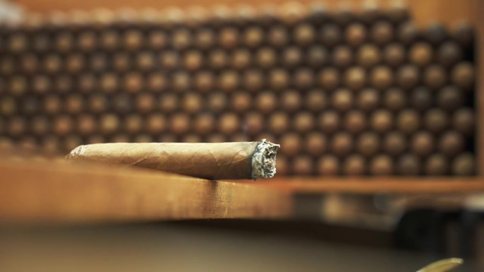在一个工厂的模糊背景中，在木架子上的一堆手卷雪茄上，冒烟的雪茄的近距离运动