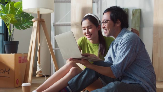 亚洲快乐的年轻夫妇在新公寓休息期间坐在家中装修配件，家庭搬迁装修室内概念，幸福夫妇粉刷墙壁