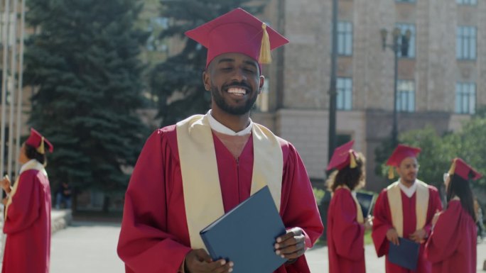 自信的非洲裔美国男学生手持文凭站在毕业砂浆板上的慢动作肖像