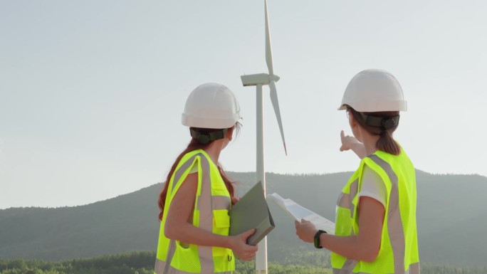 女性工程团队证实了风能作为一种环保能源的重要性。妇女们戴着头盔，戴着眼镜，手里拿着敲灯的信号胶，手里