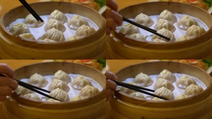一个成年人用筷子夹小笼包的特写镜头，小笼包是一种蒸熟的中国饺子，从一个热的竹制蒸笼托盘里夹出来