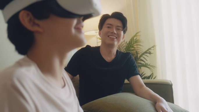 亚洲男孩戴着虚拟现实头戴式耳机和动作，在家里和他的父亲一起玩。
