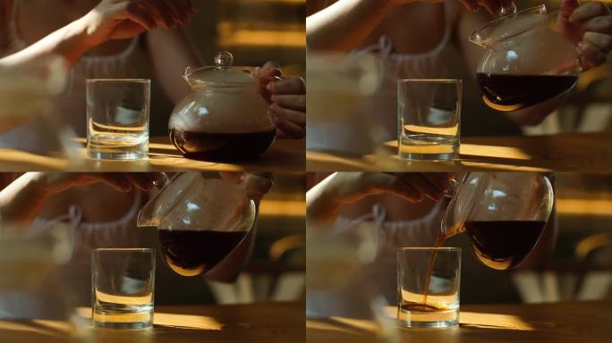 女士用杯子从玻璃杯里倒咖啡。近距离视频，女性手倒新煮的滴漏咖啡在玻璃杯坐在咖啡馆。制备咖啡的替代方法