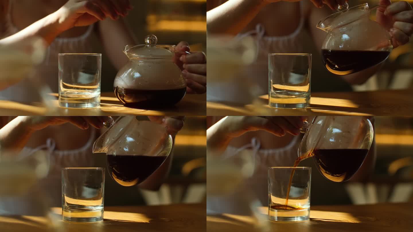女士用杯子从玻璃杯里倒咖啡。近距离视频，女性手倒新煮的滴漏咖啡在玻璃杯坐在咖啡馆。制备咖啡的替代方法