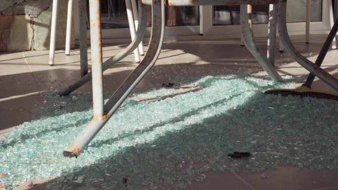 扫地扫帚移动碎玻璃堆在地板上的特写。在露台上的阳光下清理残羹剩饭。