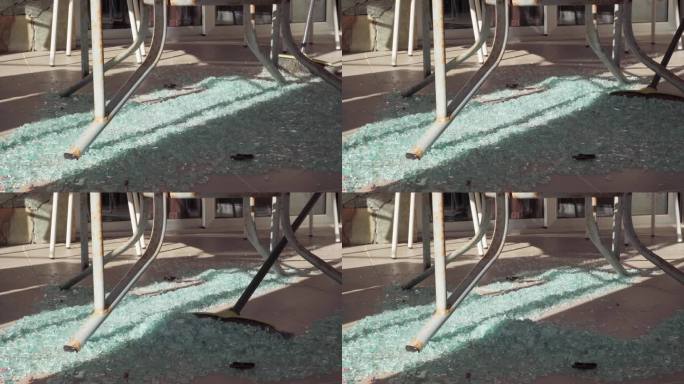 扫地扫帚移动碎玻璃堆在地板上的特写。在露台上的阳光下清理残羹剩饭。