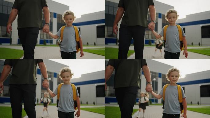 可爱的白人男孩牵着父亲的手走过校园，爸爸和儿子的肖像