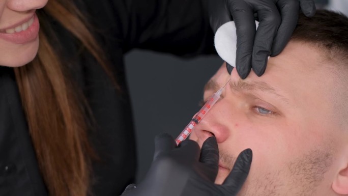 一位近距离的美容师在一位年轻英俊男子的面部皮肤上注射恢复活力的药物。