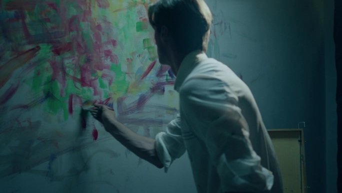 有吸引力的艺术家在他的艺术工作室的墙上做当代绘画，他拿起画笔，在画上添加了一些油画色彩