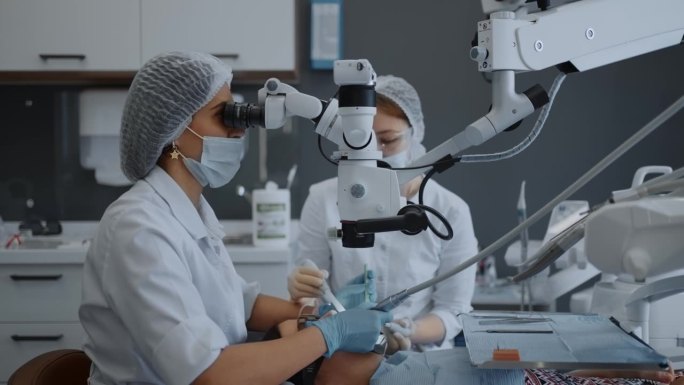 专业女牙医使用现代设备进行牙科手术，看操作显微镜
