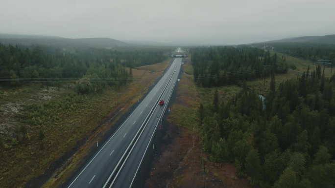 雨天行驶在森林间高速公路上的红色旅行SUV鸟瞰图