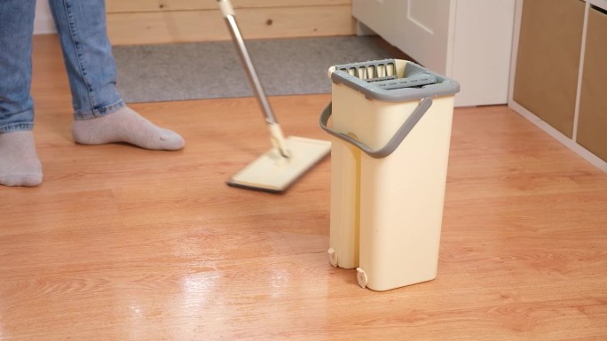 一个男人把拖把塞进桶里，洗地板。老公持家保洁理念