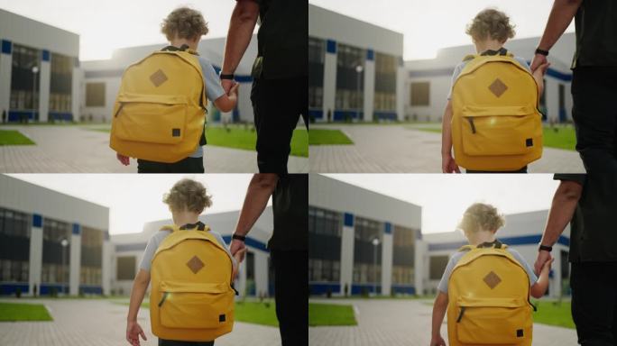 可爱的小男孩背着黄色的学校背包，牵着爸爸的手，往学校走