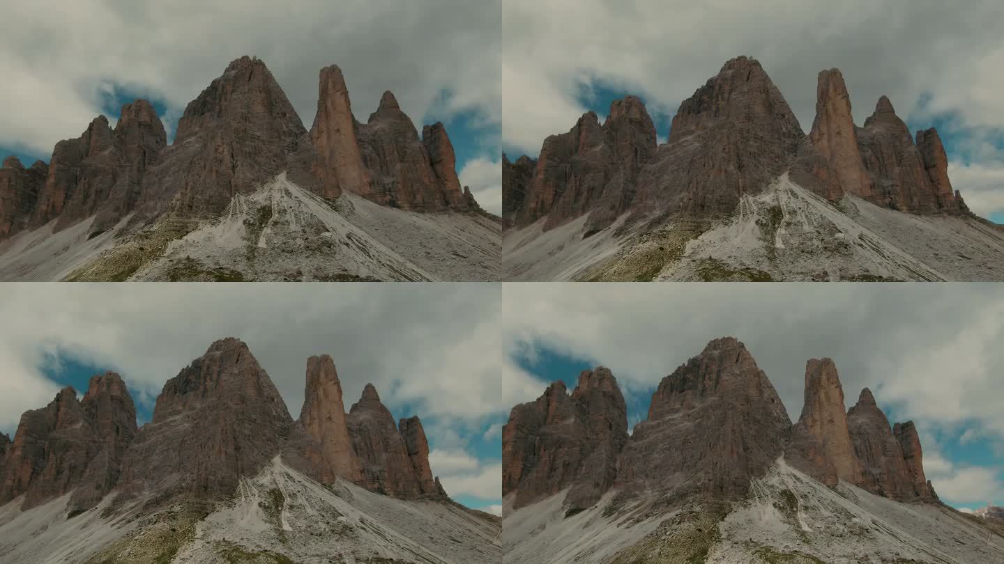 跟踪无人机拍摄，背景是高耸陡峭的岩石山脉和部分多云的天空，电影色彩等级