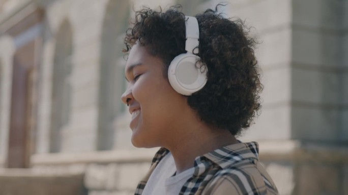 欢快的非裔美国妇女在城市外面戴着耳机听音乐跳舞的慢动作肖像