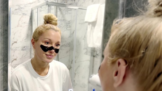 女人在浴室里照镜子，照顾自己的皮肤。洁面面膜、面膜、痘痘及油性肌肤。