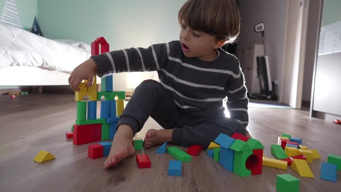 孩子在地板上玩积木。孩子不小心摧毁塔的生活镜头。一个小男孩在卧室里玩耍