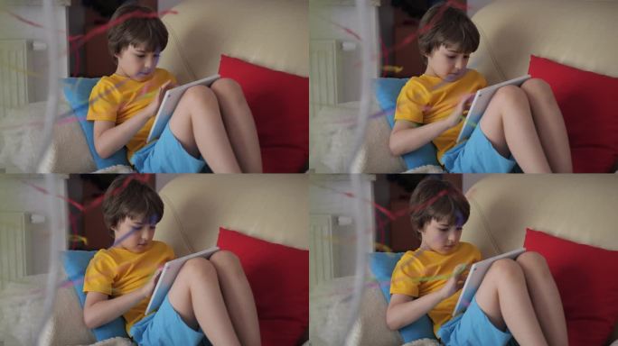 在炎热的夏天，男孩坐在沙发上，坐在风扇旁边，用平板电脑浏览社交媒体。孩子在炎热的天气里在风扇旁玩平板
