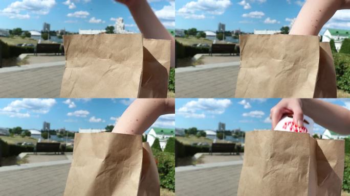 一个女人坐在公园里，从纸袋里拿出一份快餐