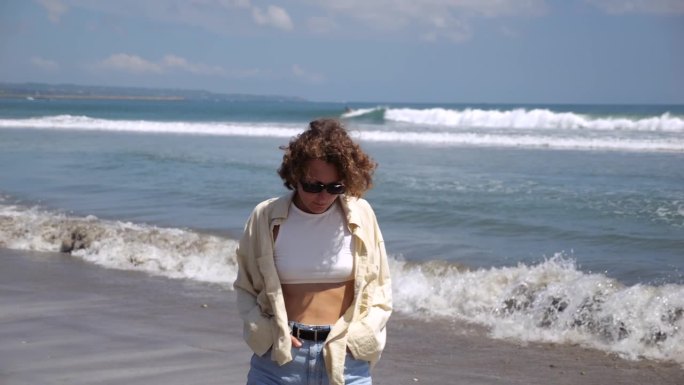 女人低头，沿着海滩散步，思考着生命的意义。戴着墨镜的卷发女孩转向大海，思考生命的意义。散步有助于思考