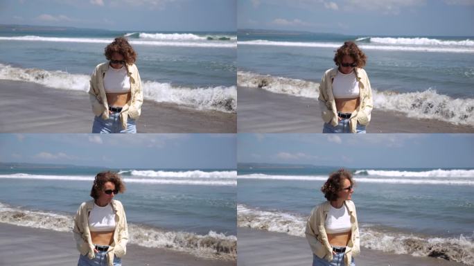 女人低头，沿着海滩散步，思考着生命的意义。戴着墨镜的卷发女孩转向大海，思考生命的意义。散步有助于思考