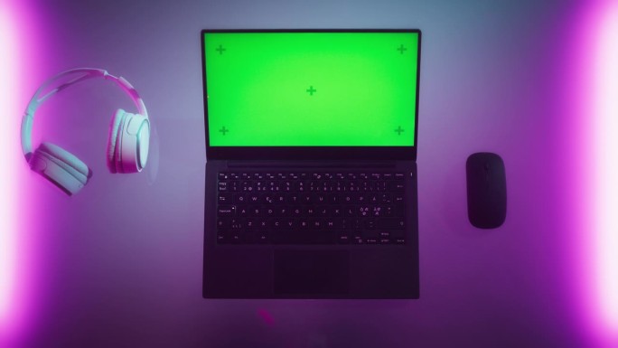 笔记本电脑的俯视图，模拟绿屏Chromakey显示器与运动跟踪器站在霓虹灯桌子旁边的无线鼠标和耳机。