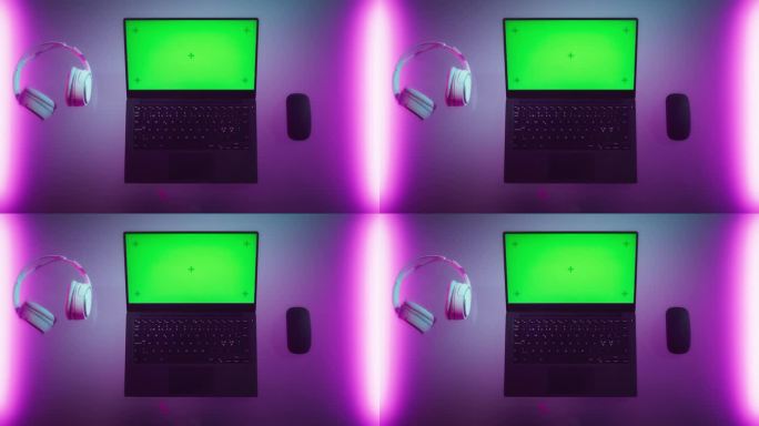 笔记本电脑的俯视图，模拟绿屏Chromakey显示器与运动跟踪器站在霓虹灯桌子旁边的无线鼠标和耳机。