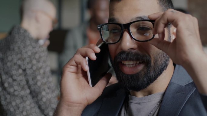 一个兴高采烈的中东人在办公室里用手机讲话，面带微笑的特写