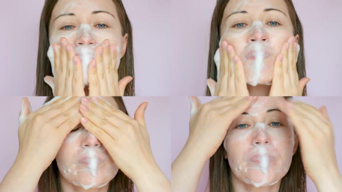 一名年轻女子将洁面泡沫涂抹在脸上(特写，背景为粉红色)。