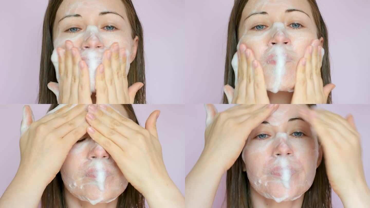 一名年轻女子将洁面泡沫涂抹在脸上(特写，背景为粉红色)。