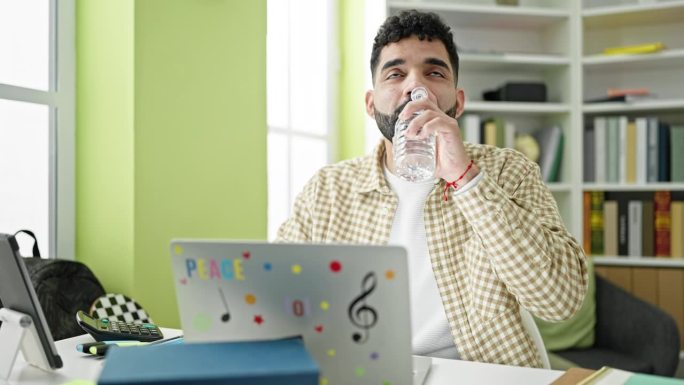 年轻的西班牙裔学生在图书馆大学用手提电脑喝水