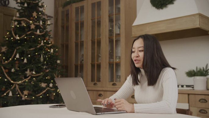 圣诞节期间，一名亚洲妇女在笔记本电脑上的视频电话会议上打招呼