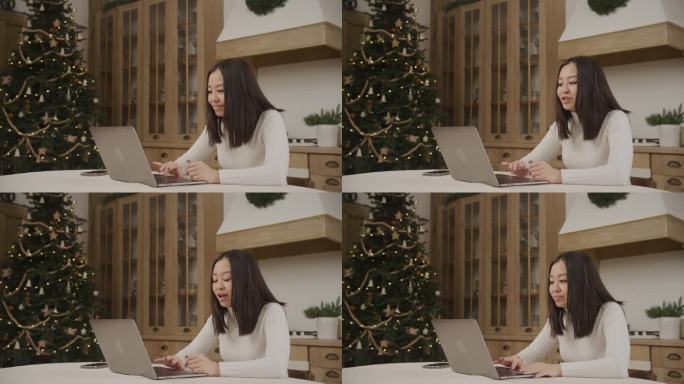 圣诞节期间，一名亚洲妇女在笔记本电脑上的视频电话会议上打招呼